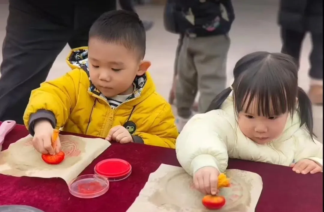 两名幼儿在非遗拓印活动中专注地给年画上色